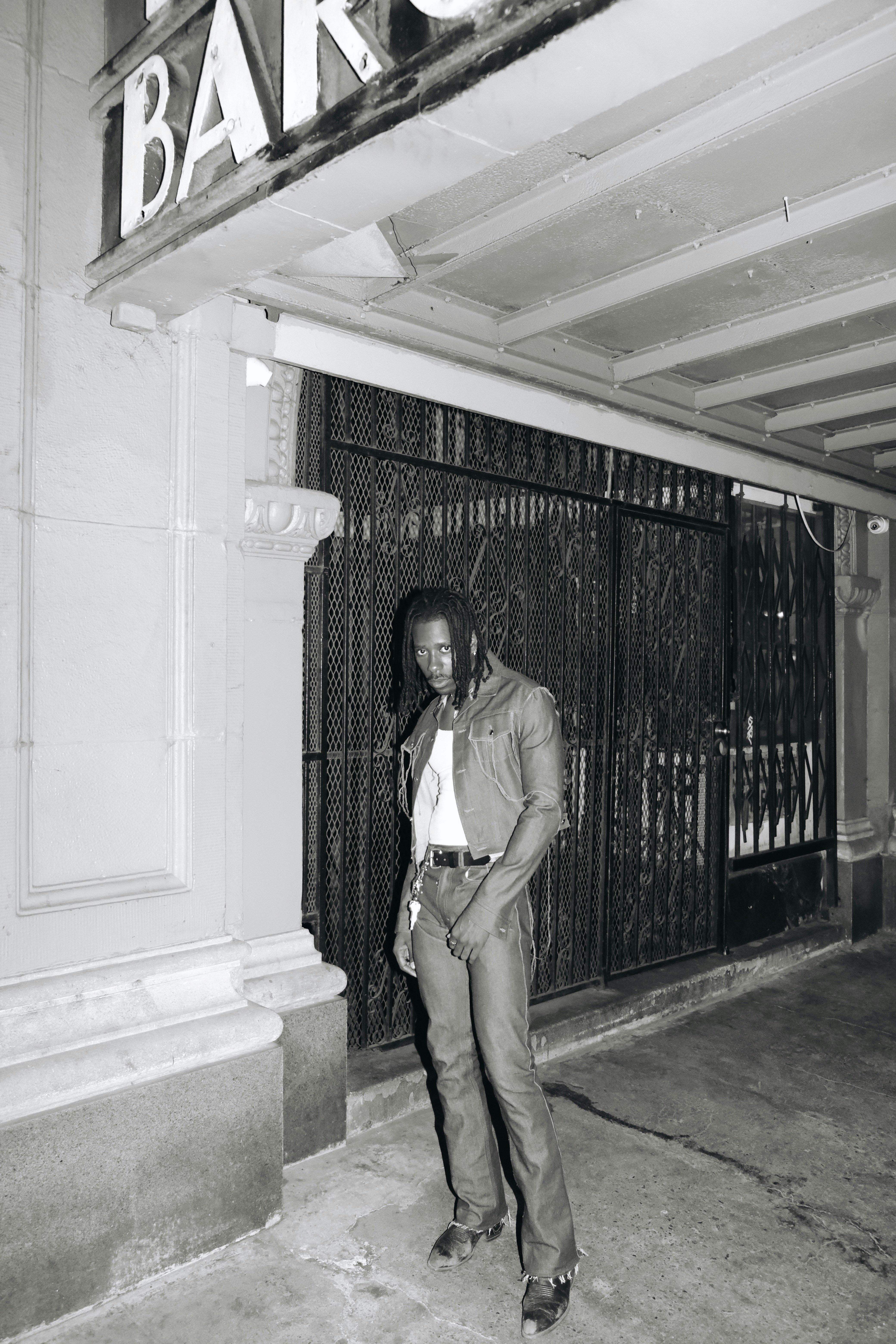 man in brown button up shirt and brown pants standing near black metal gate during daytime